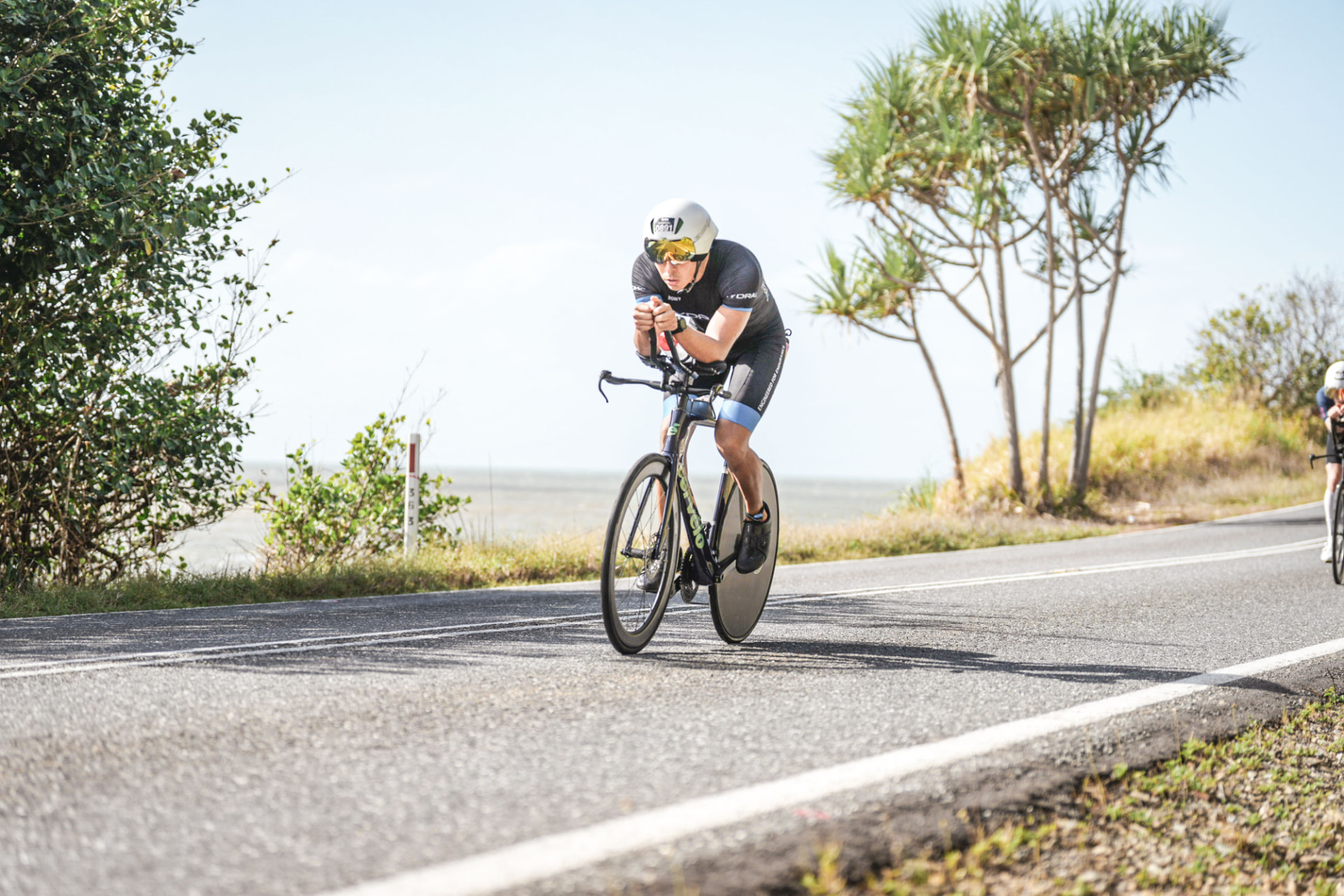 Triathlete in aero position on a time trial bike racing along a coastal Australian road, carrying race bottles mixed with carbs and sodium